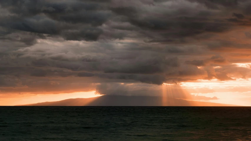 sunset with large grey clouds over ocean and island in distance