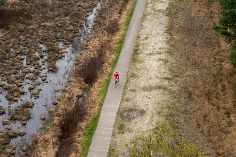 a cyclist rides in a red jacket along the riverbank