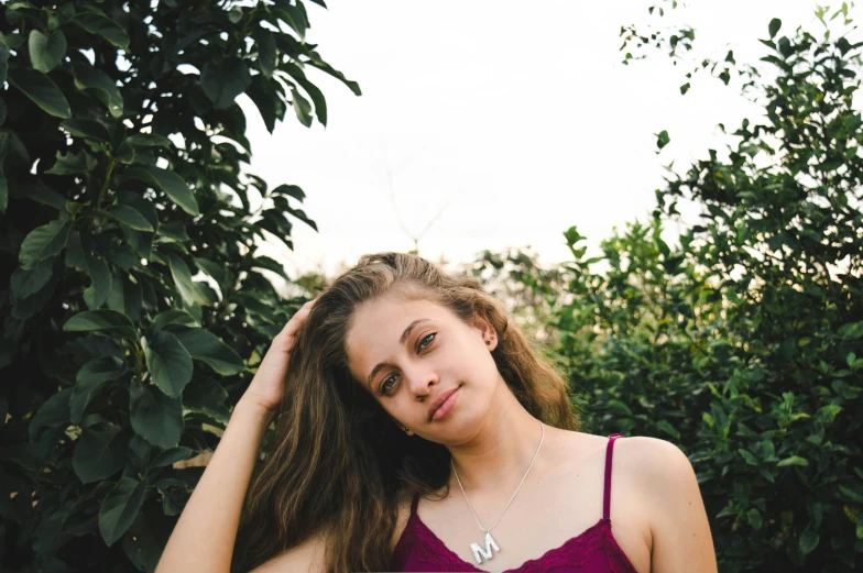 a woman wearing a maroon shirt standing by some trees