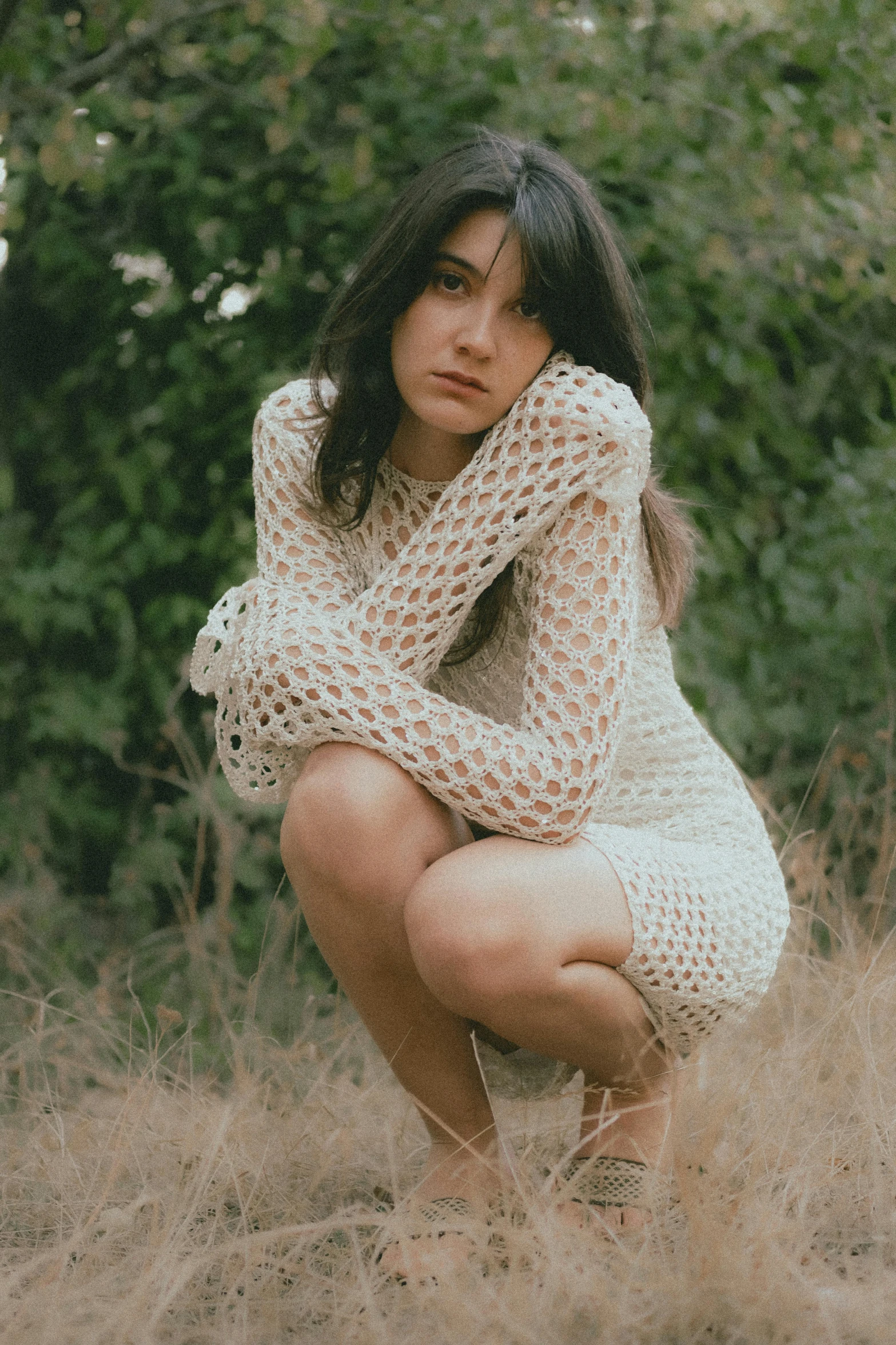 a girl kneeling in some grass next to a bush