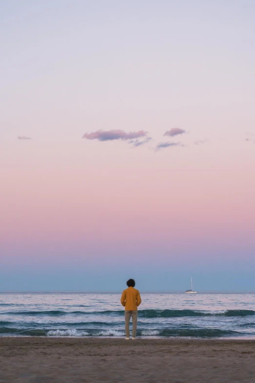 a man is standing in the beach at sunset looking towards the ocean