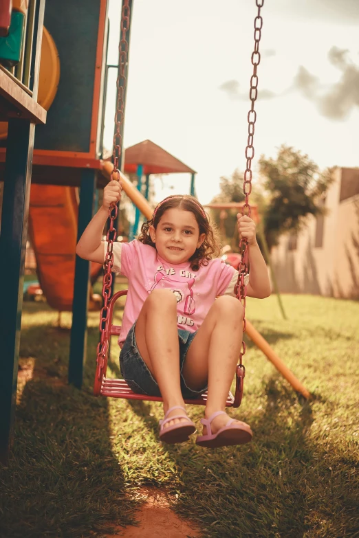 the girl is sitting on a swing at the park