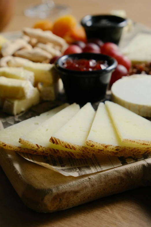 cheese slices sit on wooden  board with a bowl of sauce