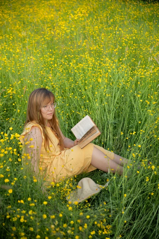 a girl sitting in a field of grass reading a book