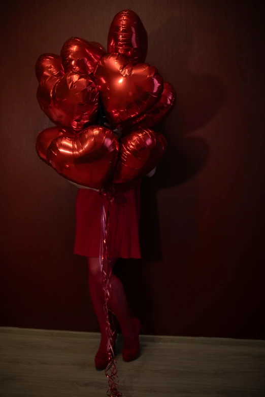 a girl in a red dress holds a red bunch of balloons