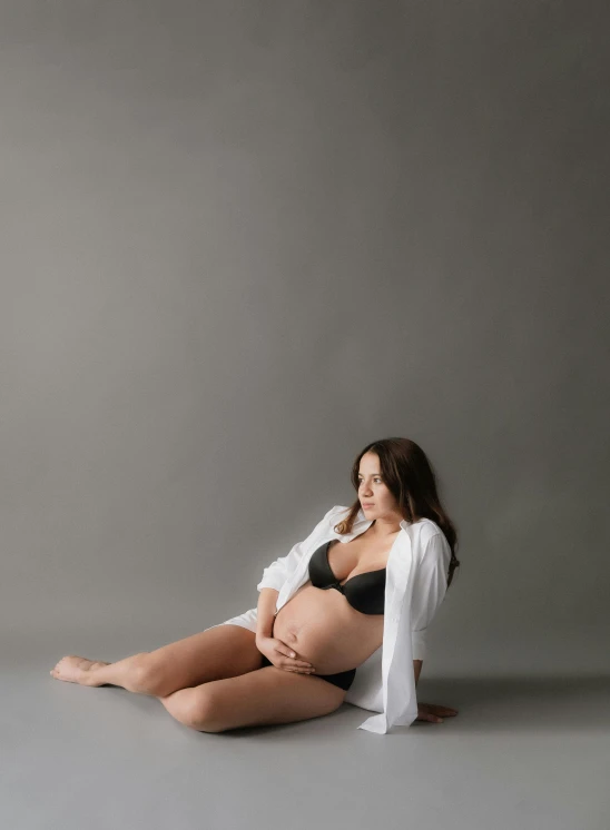 a pregnant woman sits on a gray surface