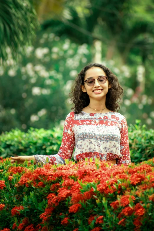 a girl wearing glasses and standing in a flower garden with red flowers