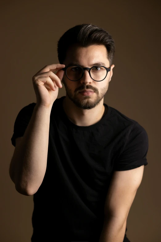 man with round glasses leaning against a wall