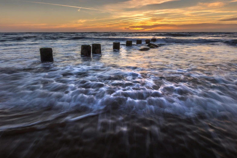 the waves come ashore in front of an orange, purple and blue sunset