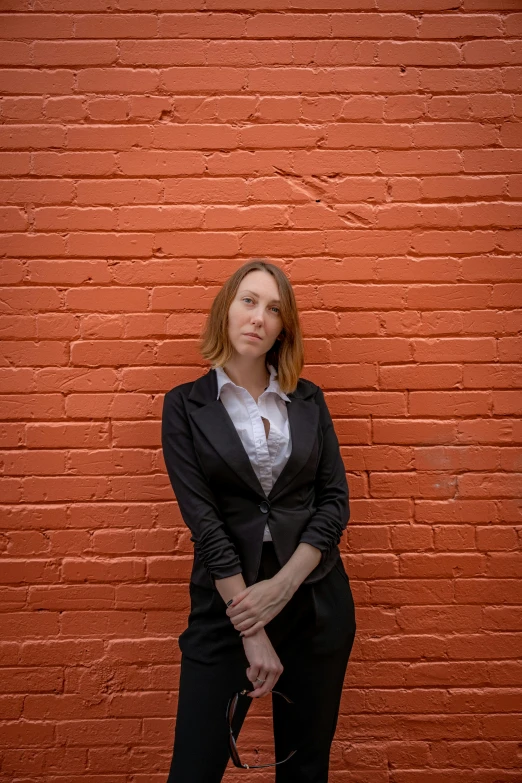 a woman in a suit stands against a brick wall