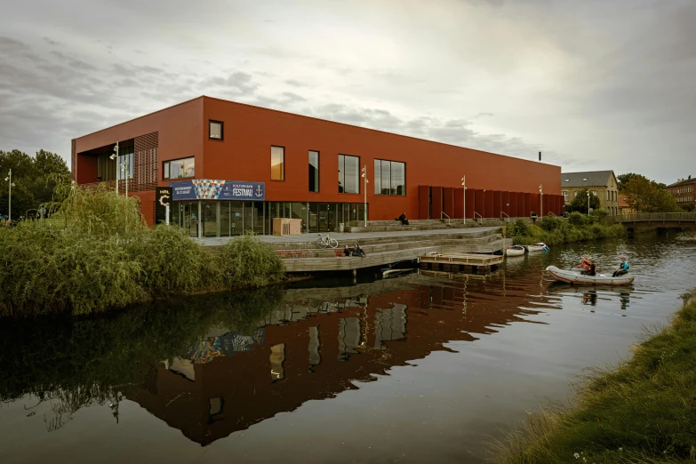 an old red building sitting on the shore with a boat floating in the water