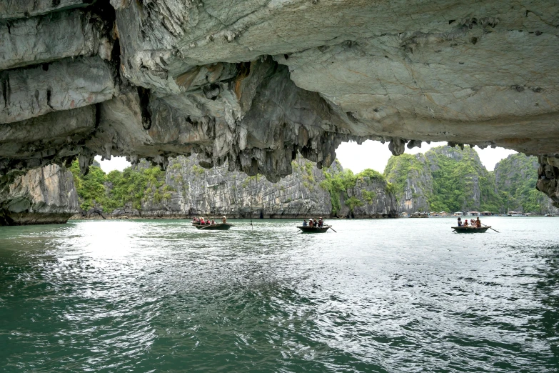 people in small boats on the water beneath large rocks