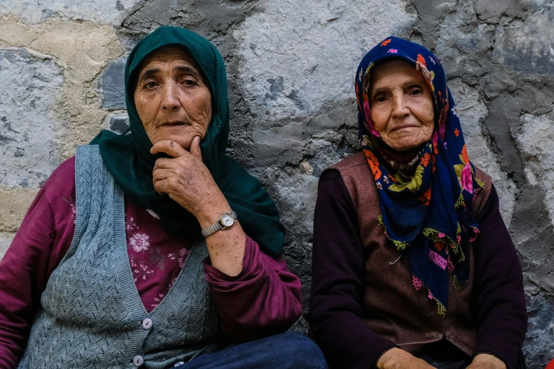 two women sit by a wall with their backs to one another