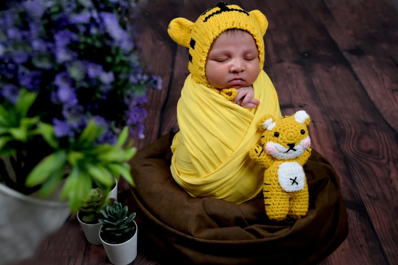 a baby wrapped in a yellow blanket next to some flowers