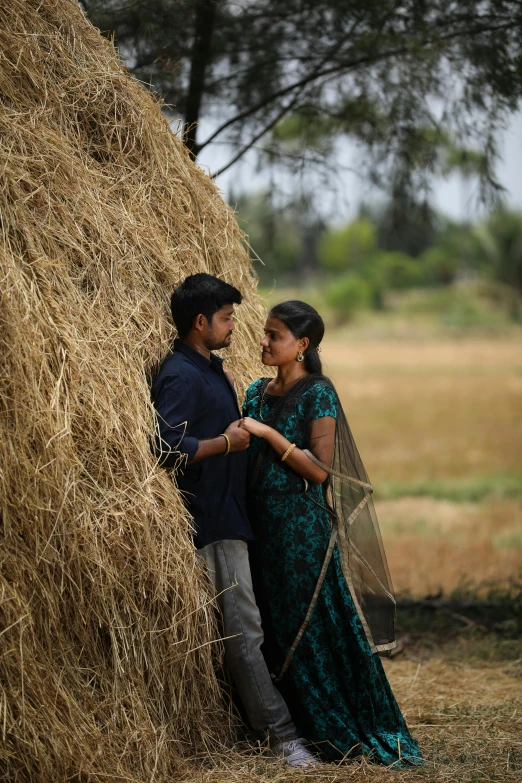 an indian couple posing next to a pile of hay