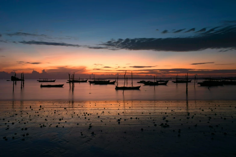 several boats are moored on the beach at sunset