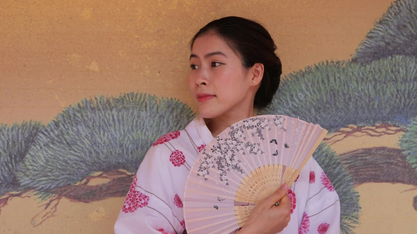 a woman is holding her own fan near wall painting