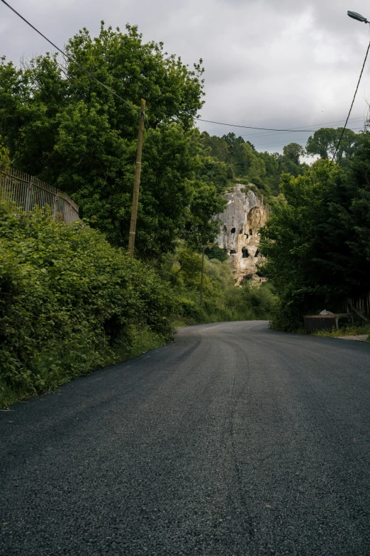 a black asphalt road with a rock building and trees lining the side