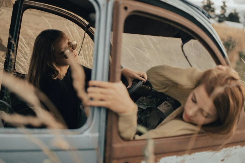 a woman sitting in a car as a young woman holds the door handle