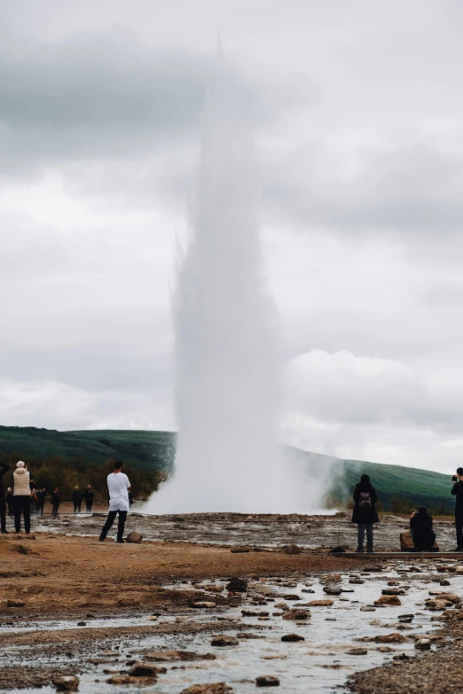 people stand near a geyser in the dirt