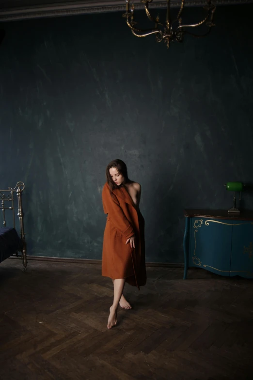 a woman in a long coat posing by a chair