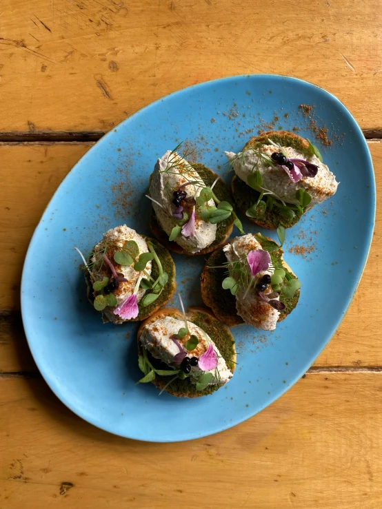 four small sandwiches on a blue plate with toppings