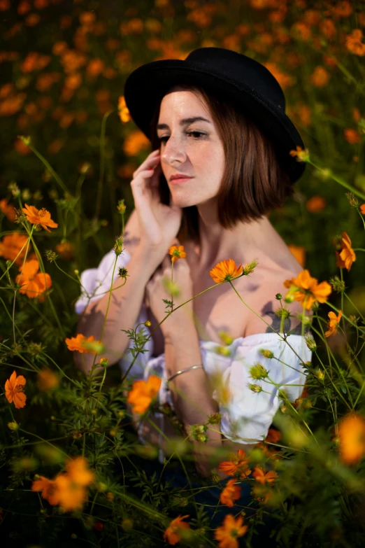 a woman in a hat and flowers has her hands on her ears