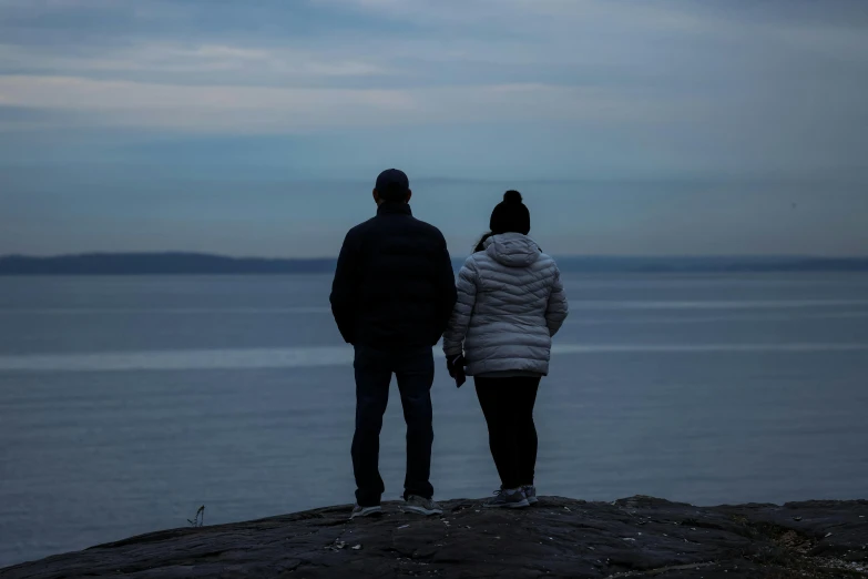 two people standing on the shore watching the ocean