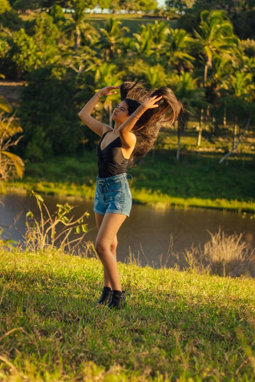 a young woman wearing short shorts is holding a large hair back and looking off into the distance