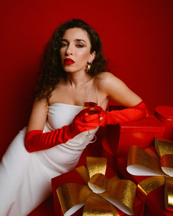 a woman in a white dress and red gloves near a box filled with gold presents