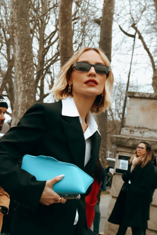 a woman with sunglasses on, holding a blue purse