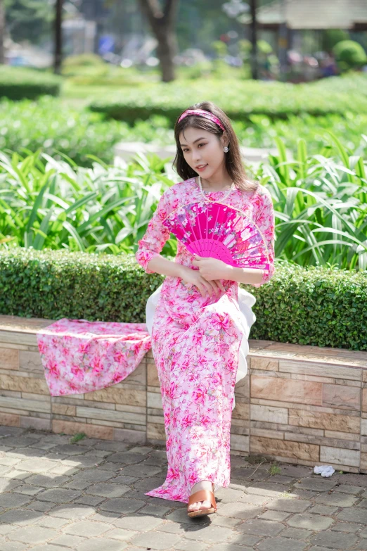 an oriental woman in a red and pink patterned dress holds her fan