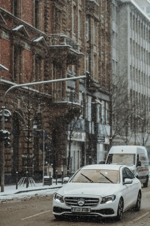 two cars driving down a street with snow falling on it