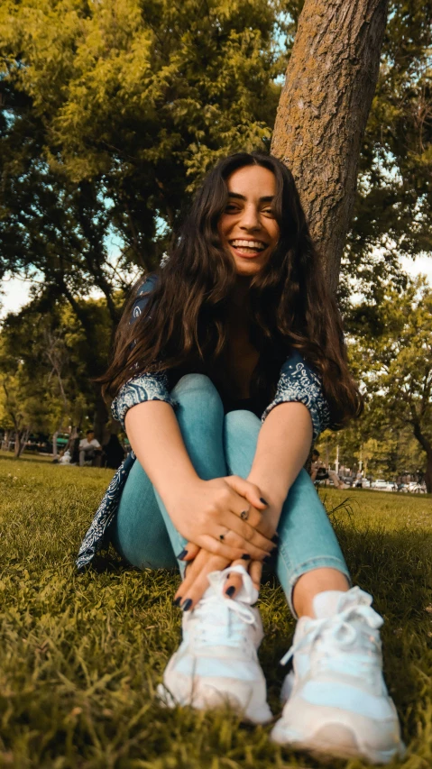 a woman with long hair sitting in the grass next to a tree