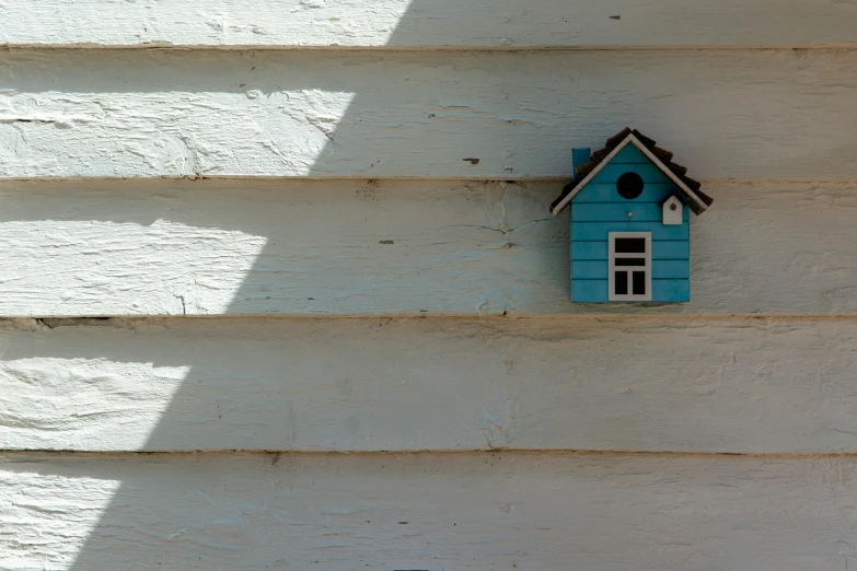 the small blue birdhouse is attached to a wooden house