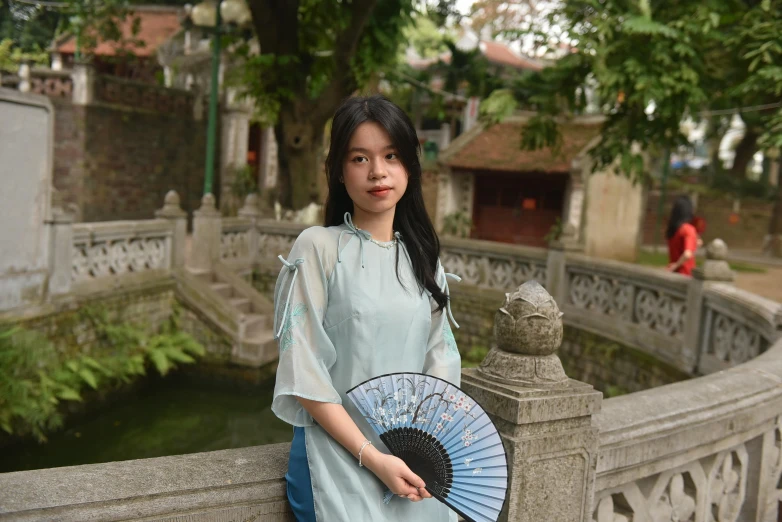 a girl poses next to a fence with a blue fan