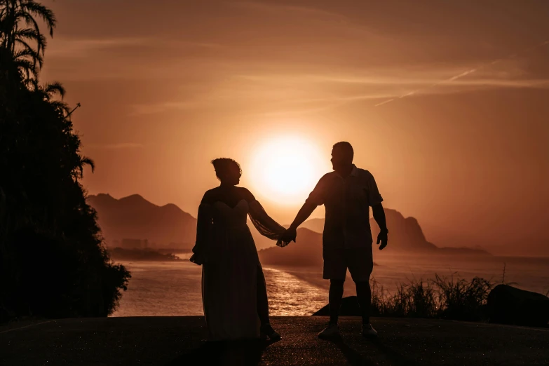 two people hold hands with the sun setting in the background