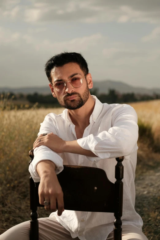 a man sits in a chair, wearing sunglasses and looking off into the distance