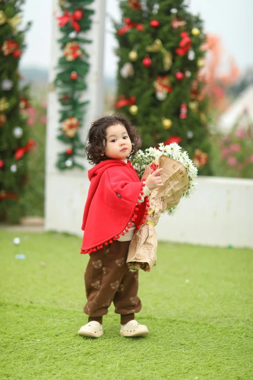 a small girl in red jacket holding flowers in front of trees