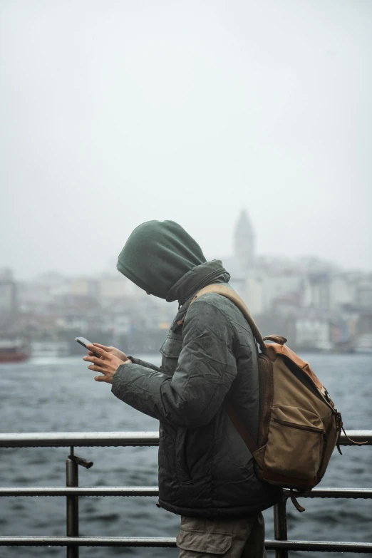 man in jacket standing on waterfront checking his cell phone