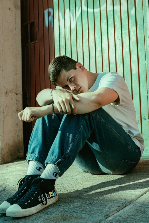 a young man is sitting on the ground with his hands folded