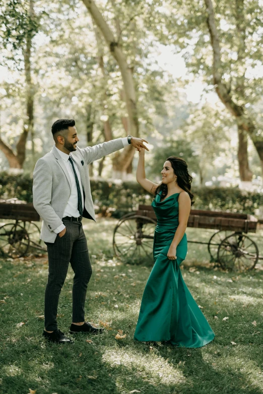 a woman in a green dress is holding her arm up next to a man in a white blazer