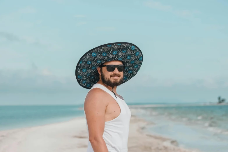 a man wearing a hat and sunglasses standing on the beach