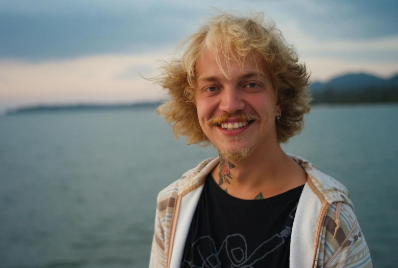 a man with blonde hair and beard standing by the water