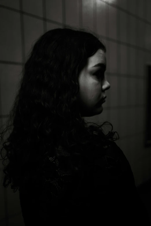 a girl is standing by a tile wall in a dimly lit bathroom