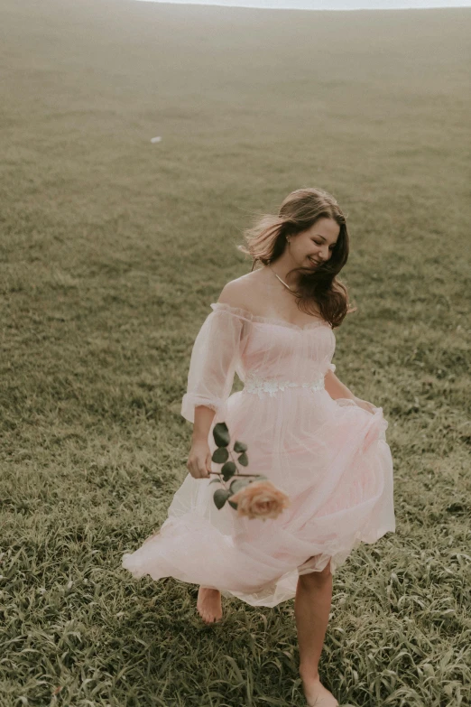 a woman walking in a field, wearing a pink dress