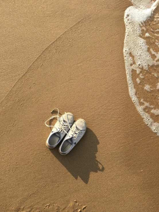 a pair of shoes laying on the sand next to water