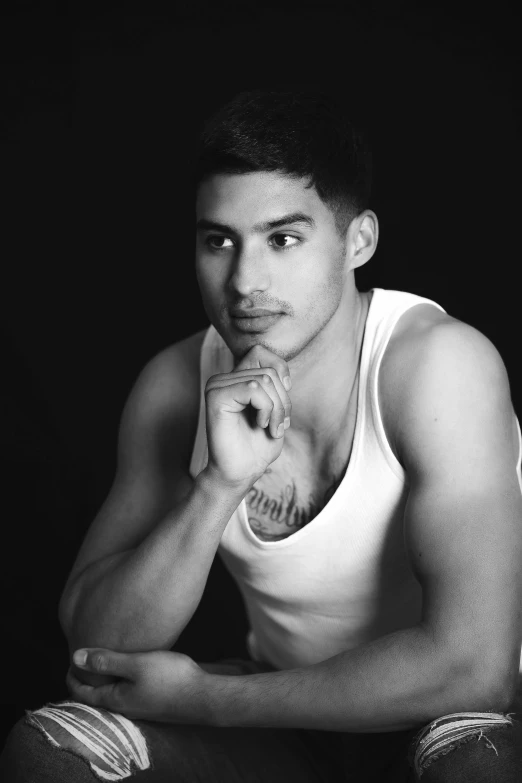 young man with black hair and white tank top seated and leaning on his elbows