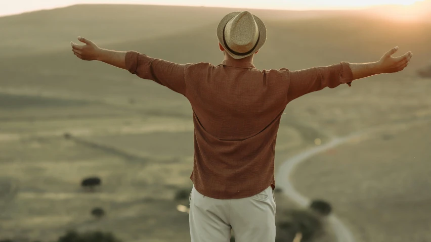 a man wearing a brown sweater and white pants is standing in the dirt