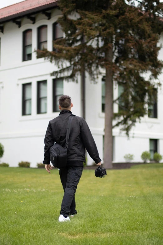 man in black jacket walking out to grassy area next to white building